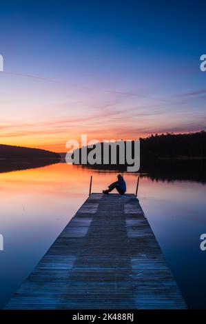 Uomo seduto sul molo all'alba Foto Stock