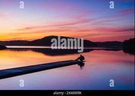 Uomo seduto sul molo all'alba Foto Stock