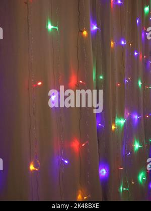Multicolor Natale o Capodanno ghirlanda di LED diversi colori luci su tenda in cotone beige, arredamento per la casa. Foto verticale. Messa a fuoco selettiva. Foto Stock