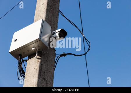 La telecamera a circuito chiuso è montata su un palo stradale in cemento sotto il cielo blu. L'osservazione CCTV è in corso Foto Stock