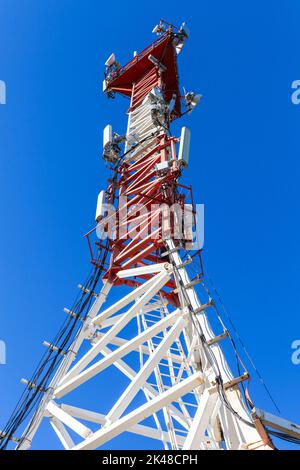 La torre di telecomunicazione bianca rossa con dispositivi radio è sotto il cielo blu in una giornata di sole Foto Stock