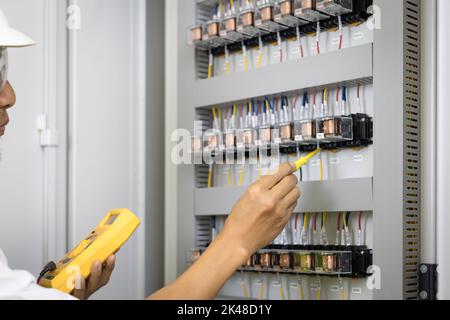 Un elettricista maschio lavora in un quadro elettrico, morsettiera elettrica. Pannello di controllo con contattore magnetico e relè di sovraccarico, misurazione della tensione in ma Foto Stock