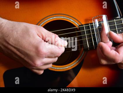 Uomo che suona una chitarra acustica con uno scivolo di vetro. Primo piano delle mani. Foto Stock