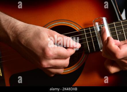 Uomo che suona una chitarra acustica con uno scivolo di vetro. Primo piano delle mani. Foto Stock