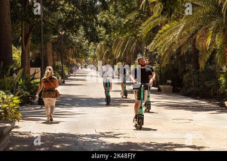 I giovani che hanno fatto il kick scooters elettrico nel parco cittadino, Paseo del Parque a Málaga, in Spagna. Foto Stock