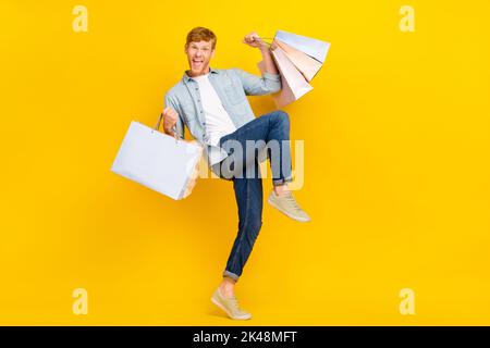 Foto a grandezza naturale di un bel ragazzo fortunato vestito blu jeans jeans jeans jeans jeans tenere borse celebrando i nuovi vestiti isolati su sfondo di colore giallo Foto Stock