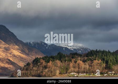 Bella vista sul paesaggio invernale lungo Loch Leven verso montagne innevate in lontananza con il cielo drammatico Foto Stock