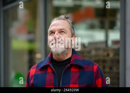 Uomo di mezza età con un sudicio mazzetto in una giacca rossa e blu nello stile di un lumberjack si trova in una strada commerciale Foto Stock