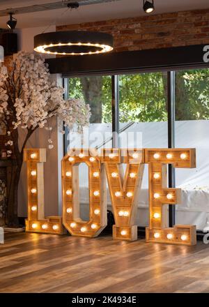 Belle lettere d'amore in legno con luci illuminate nel luogo del matrimonio. Foto Stock