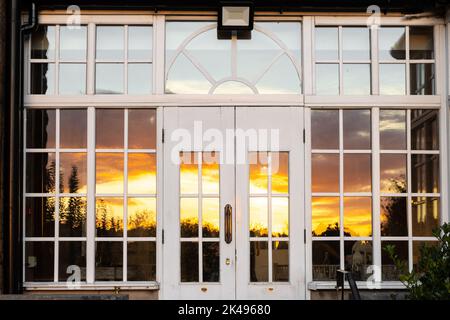 Bellissimo tramonto arancione e giallo fuoco riflesso in legno ornato finestre bianche incorniciate Foto Stock