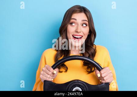 Ritratto fotografico di affascinante giovane donna tenere auto timone guardare spazio vuoto vestito elegante abito giallo isolato su sfondo di colore blu Foto Stock