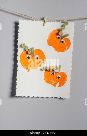 Stampe di zucca di Halloween per bambini con disegno appeso alla corda sulla parete grigia. Decorazioni fai da te fatte a mano con bambini per le vacanze. Verticale Foto Stock