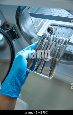 Primo piano della mano nei guanti con contenitore con strumenti odontoiatrici Foto Stock