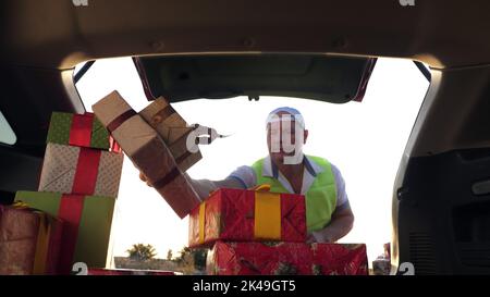 servizio di consegna. deliveryman in maschera protettiva. il corriere scarica le scatole. scatole regalo in auto. pacchi ben avvolti. vista dall'interno dell'auto. concetto di donazione, beneficenza o consegna. Foto di alta qualità Foto Stock