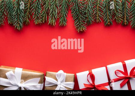 Sfondo creativo di Natale con scatole regalo di Natale e ramoscelli di pino su sfondo rosso. Disposizione piatta, vista dall'alto, spazio di copia Foto Stock