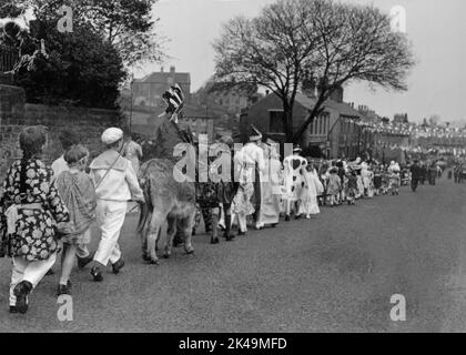 I bambini in abiti eleganti, tra cui un ragazzo in sella a un asino, camminano in processione il 6 maggio 1935, il Silver Jubilee Day di Re Giorgio V, lungo una lunga strada diritta (probabilmente Wakefield Road), addensata di bandiere e accatastata a Denby Dale nello Yorkshire occidentale, Inghilterra, Regno Unito. Foto Stock