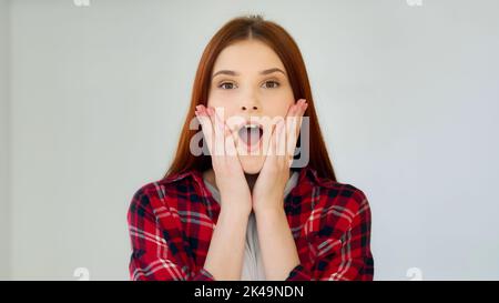 Sorpresa zenzero ragazza studente adolescente sentirsi bene shock ammirazione femmina faccia eccitata vincitore dice wow reazione positiva tiene la testa dalle mani di successo Foto Stock