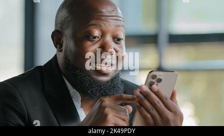 Felice uomo d'affari afroamericano alto bello bearded adulto uomo insegnante allenatore dipendente leggere buone notizie sul sito web chattando l'uso di app mobile Foto Stock