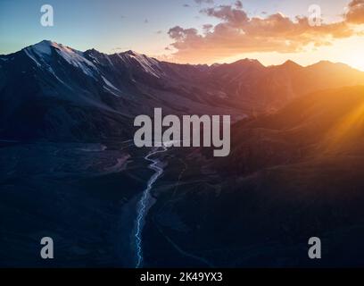 Splendido scenario delle montagne con ghiacciaio di neve e fiume in silhouette al tramonto arancione cielo Almaty, Kazakistan. Outdoor e concetto di escursioni, aer Foto Stock
