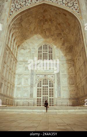 Un colpo verticale di un uomo seduto all'ingresso della tomba del Taj Mahal. Agra, India. Foto Stock