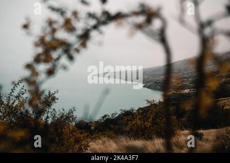 paesaggio tra i rami del bosco vicino al lago e la montagna con una strada in una giornata grigia cupa senza sole e scarsa visibilità Foto Stock