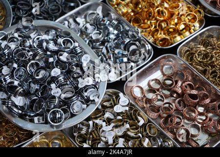 Piastre metalliche piene di una varietà di anelli in un mercato Foto Stock