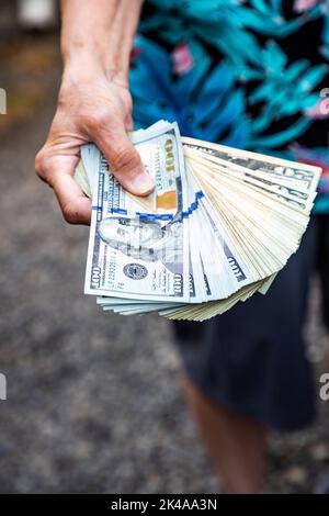 Mano che si estende tenendo una pila di valute - dollari cento fatture Foto Stock
