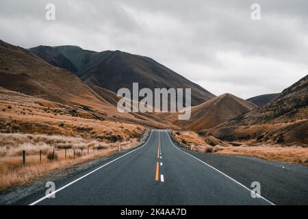 lunga strada stretta senza traffico che si perde tra le montagne solitarie in un paesaggio desolato senza alberi con un sacco di nubi grigie, monte cuoco Foto Stock