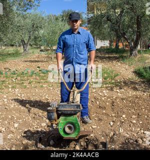 Contadino con un timone mentre coltiva una terra per la coltivazione dell'orto. Preparazione di suolo fertile Foto Stock