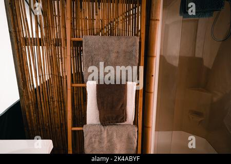 asciugamani puliti e morbidi disposti sui gradini della scala di legno accanto alla parete di canne di bambù in un bagno pulito nella tenda Foto Stock