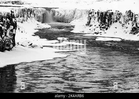 Cascata Selfoss con il fiume Jökullsa a Fjöllum, pareti rocciose ghiacciate e innevate e litorale, foto in bianco e nero, Islanda settentrionale Eyestra, i Foto Stock