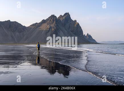 Turista alla spiaggia di lava nera, spiaggia sabbiosa e mare, montagne Clifatindur riflesso in acqua, Eystrahorn e Kambhorn, punta Stokksnes, montagna Foto Stock