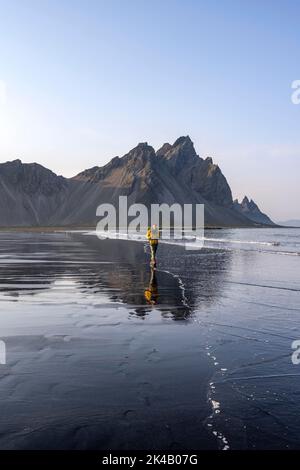 Turista alla spiaggia di lava nera, spiaggia sabbiosa e mare, montagne Clifatindur riflesso in acqua, Eystrahorn e Kambhorn, punta Stokksnes, montagna Foto Stock