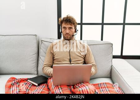 Giovane uomo bello con barba che indossa la cuffia operatore che lavora da casa scettica e nervosa, insensata a causa del problema. Persona negativa. Foto Stock