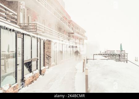 Il personale dell'albergo pulisce la neve all'aperto in condizioni di neve con il trattore. Vacanze invernali e problemi di neve dopo una forte nevicata Foto Stock
