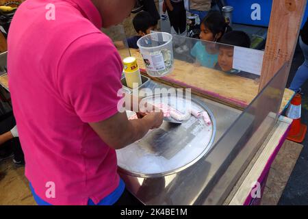 I bambini guardano un venditore di cibo che li rende un dessert di gelato alla fragola al festival di strada di San Gennaro a New York Foto Stock