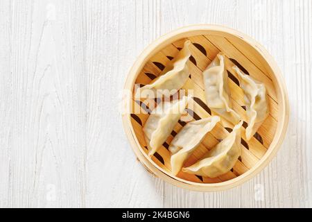 gyoza, wonton wrapper farciti con maiale e cavolo in bambù a vapore su tavolo di legno bianco, vista orizzontale dall'alto, piano di giacitura, spazio libero Foto Stock