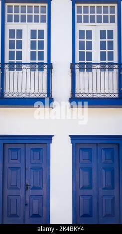 Facciata casa coloniale con finestre con pannelli in legno bianco con finiture blu cobalto e porte in legno blu cobalto a Sabará, Minas Gerais, Brasile Foto Stock