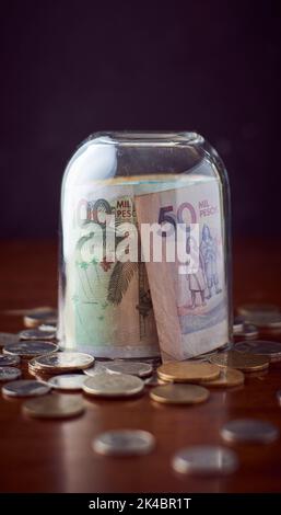 Una tazza di vetro di chiusura sul colombiano peso moneta in contanti su un tavolo di legno con monete, con sfondo scuro Foto Stock