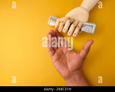 La mano di un uomo chiedeva denaro da una mano di legno che teneva una banconota Foto Stock