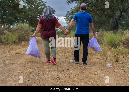 coppia di ambientalisti con sacchi di spazzatura che camminano mano in mano lungo una strada piena di spazzatura Foto Stock