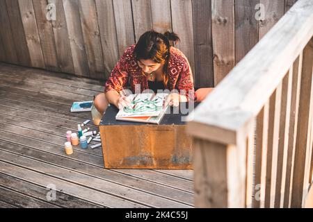 Giovane ragazza seduta a gambe incrociate dipingendo una tela Foto Stock