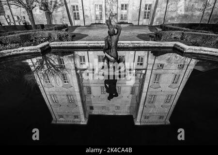 Una foto in scala di grigi di statua in fontana con il riflesso della facciata dell'edificio sullo sfondo Foto Stock