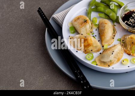 Primo piano di gnocchi asiatici, salsa di soia e bacchette su sfondo grigio Foto Stock