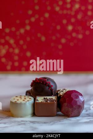 elegante dolce vita morta di cioccolatini di prima qualità su uno sfondo natalizio di rosso e oro Foto Stock