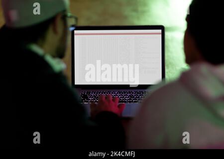 Vista posteriore di due diversi colleghi maschi che utilizzano un computer portatile con codifica sullo schermo. Codifica, programmazione e computer tecnologia immagine composita digitale. Foto Stock