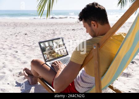 Uomo caucasico in vacanza che utilizza un computer portatile con vista della casa da telecamere di sicurezza sullo schermo. Sicurezza, sicurezza, sorveglianza e interfaccia digitale. Foto Stock