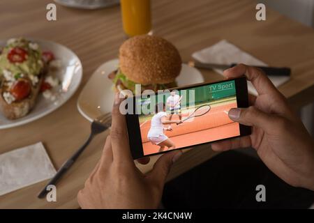 Mani dell'uomo afroamericano al ristorante guardare la partita di tennis su smartphone. Sport, competizione, intrattenimento e tecnologia concetto di digital com Foto Stock