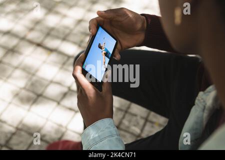 Uomo afroamericano nel parco che guarda atleta maschio gettando discus su smartphone. Sport, competizione, intrattenimento e tecnologia concetto digitale co Foto Stock