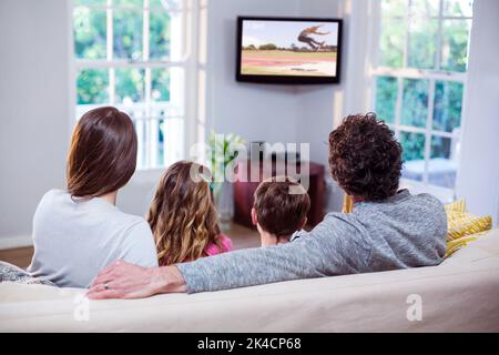 La famiglia guarda la televisione mentre si siede sul divano di casa Foto Stock